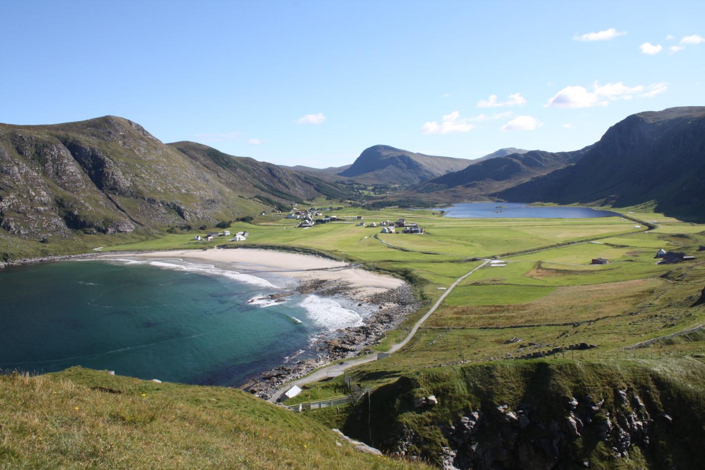 bilde av bygd ved strand, fjell og dal i bakgrunn