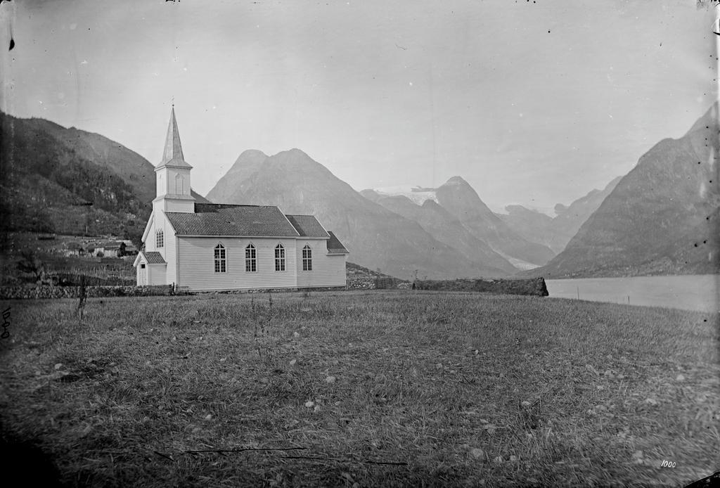 bilde i svart-kvitt av kyrkje, fjell og fjord.