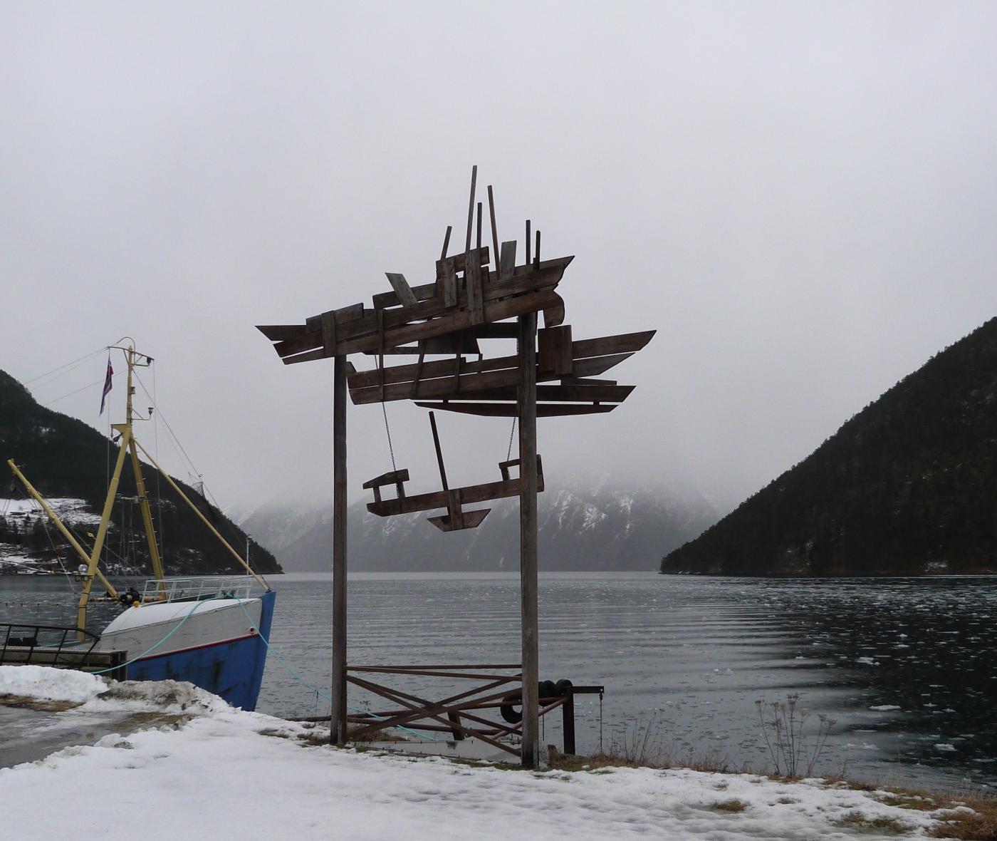 Kunstverket står attmed eit av husa som høyrer til Sogn Fjordmuseum, De Heibergske Samlinger – Sogn folkemuseum.