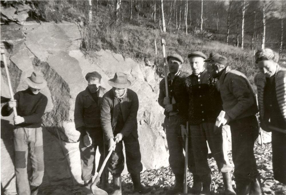 Biletet er frå veganlegget Hyllestad-Øn rundt 1959. Mykje av arbeidet vart gjort på dugnad. Både menn og kvinner var med. Biletet er teke i skjeringa i Selvika, med nokre frå dugnadsgjengen i arbeid. Vegparsellen var 10 km og knyta to bygder saman og gav mange gardar vegutløysing. Frå venstre ser vi Oskar Berge, Peder Stigrdal, Ragnvald Tonning, Kristian Berge, Godtfred Hatlem, Ingvald Sørensen og Ella Tonning. 