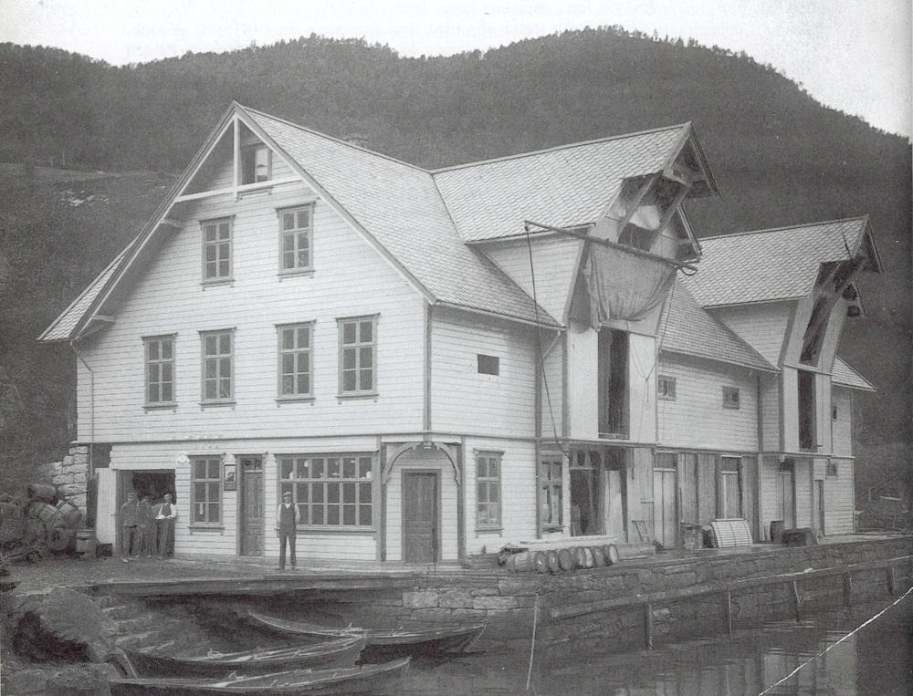 Båtstoppetaden Steinen før 1920. Vi ser ein del personar framfor huset som m.a. romma ein butikk. Tønner ligg pent stabla opp på bryggja og nokre robåtar ligg førtøydde.