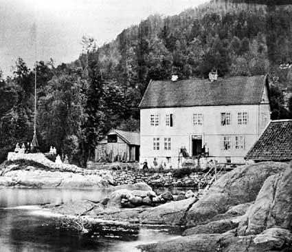 Bilete av hovudhuset i Flesje. Til venstre kring flaggstonga heitte det Skansen. Der stod det bord og stolar og dette var ein fin plass når det var godvêr og utsynet over Sognefjorden var vidt og fagert. Til høgre ser me taket på sjøbua. Ho datt ned  i 1960-åra.