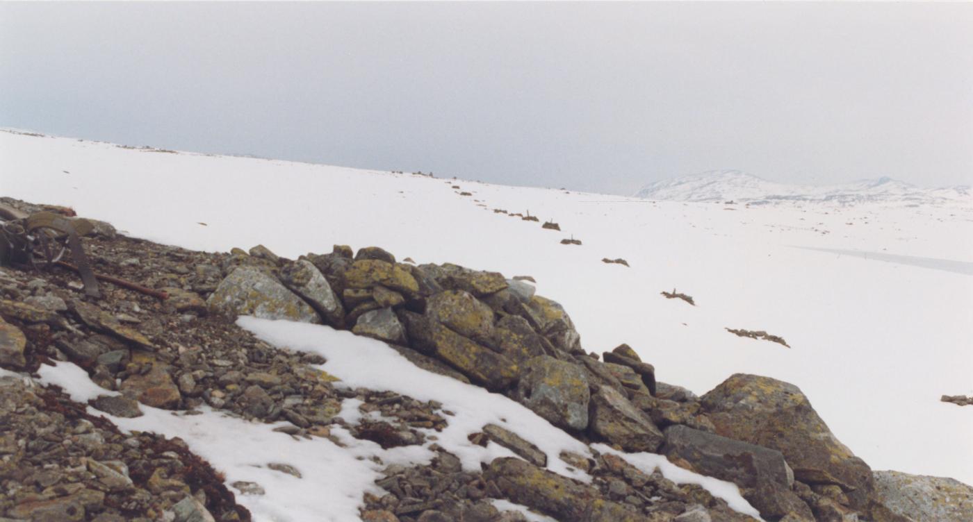 Skjerdalshøgdi sett frå vest. Nærast ser me stolpefeste frå 1859. Rekkja med stolpekar i snøen er frå fyrste omlegginga, truleg i 1863. Me ser hyttemurane i synsrandi.