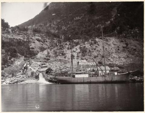 Dampskipet «Vangsnæs» til kai i Kinsedal. Båten var som ny (1904) utstyrt med snesegl til bruk på begge mastene (sjå foto av båten på Vikjabukta). Her er utstyret for segling teke bort. BT melde våren 1905 om at «Vangsnæs» hadde frakta ved frå Sogn til Bergen, «Nesten paa hver Tur.» Biletet viser mykje ved opplødd på land, - sytten lad, a 2 famnar, kan det sjå ut som.