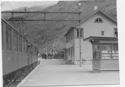 Her ser vi Flåm stasjon i 1960-åra. Bana var lenge truga av nedleggjing. I 1998 skilde NSB ut Flåmsbana og la drifta til eit samarbeidsselskap mellom anna med Aurland kommune. NSB har framleis driftsansvaret. Flåmsbana er i dag ein turistbane og står høgt på lita over turistattraksjonar. I 1920 stipulerte dei eit passasjertal på 22.000 reisande årleg, men talet var for lågt. I 1960- og 70-åra var det jamt rundt 115.000 reisande i året. Frå 1990 endra dette seg, og i 2004 var det 459.144 reisande med...