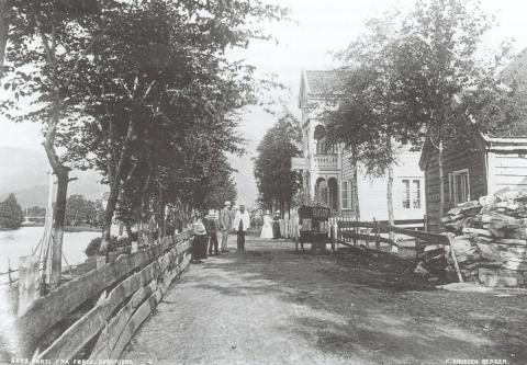 Hafstad Hotell kring 1895. Ei stove i framgrunnen og ein del folk framfor hotellet. Vi ser litt av elva Jølstra og innover mot Langebrua.