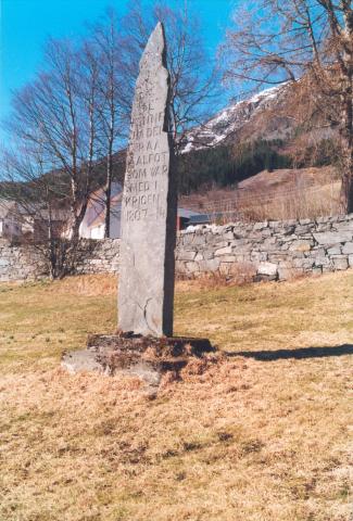 <p>Bautasteinen, av bergarten gneis, er 4,38 m over betongfundamentet. P&aring; baksida st&aring;r: 17 MAI * 1914. Harald Bruland fortel at det har vore sagt at steinen skal vera nesten like lang under jorda som over. Det kan ikkje ha vore nokon enkel transport.</p>