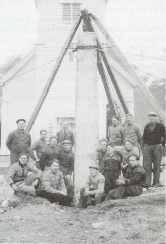 Våren 1946. Minnesteinen er komen i rett stilling ved hjelp av ein ekstra høg stubbebrytar. Fjorten mann er med på arbeidet. 
